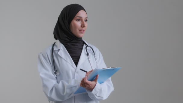 Physician specialist woman female doctor muslim therapist wear hiding hijab listen health concerns patient complaints writing notes in hospital fill medical form insurance register disease symptoms  - Кадры, видео