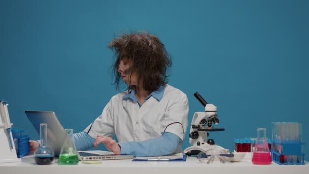 Hauska hullu naispuolinen tiedemies katselee koeputkia pöydällä - Materiaali, video