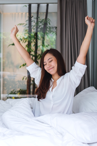 Una hermosa mujer asiática hacer estiramiento después de despertar por la mañana en una cama blanca y acogedora en casa - Foto, Imagen