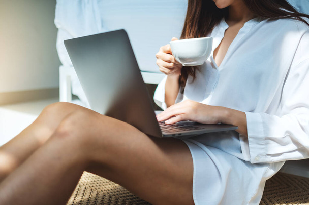 Nahaufnahme einer Frau, die einen Laptop benutzt und daran arbeitet, während sie Kaffee trinkt und zu Hause im Schlafzimmer sitzt - Foto, Bild