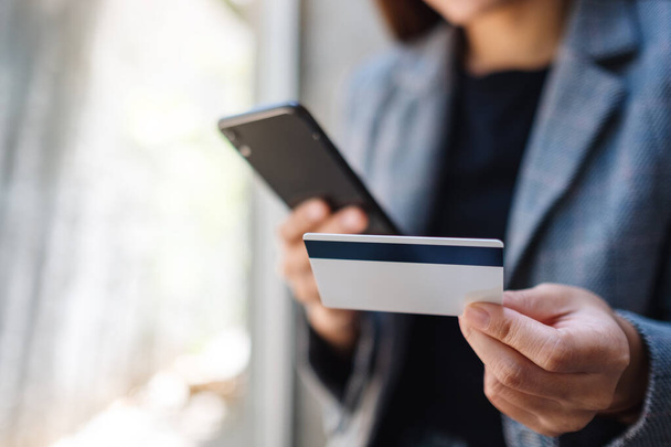 Cep telefonundan alışveriş yapan ve kredi kartı kullanan bir kadının yakın plan fotoğrafı. - Fotoğraf, Görsel