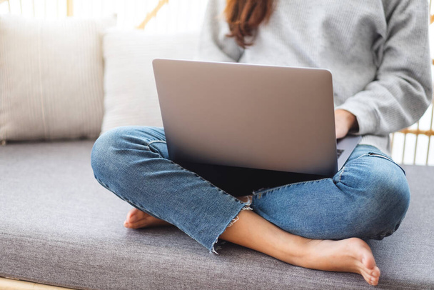 Una bella donna che usa e lavora sul computer portatile mentre è seduta su un divano a casa - Foto, immagini