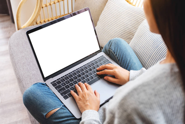 Top view mockup afbeelding van een vrouw werken en typen op laptop computer met blanco scherm tijdens het zitten op een bank thuis - Foto, afbeelding
