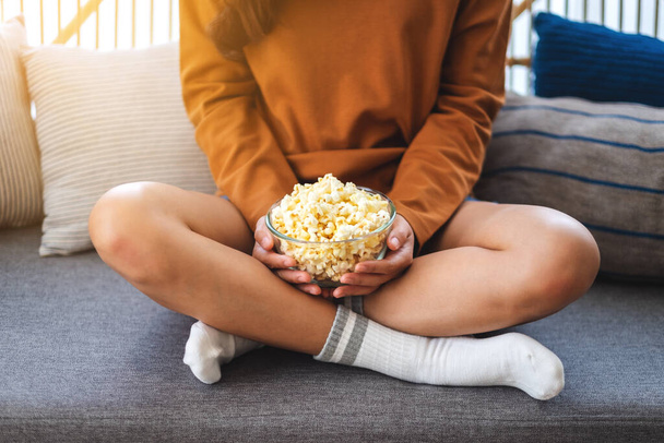 Close up image of a woman holding a bowl of pop corn while sitting on sofa at home - Photo, Image