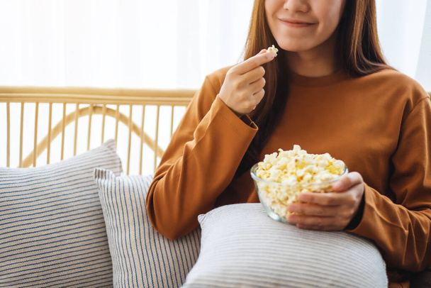 Imagen de cerca de una hermosa mujer joven sosteniendo y comiendo maíz pop mientras se sienta en el sofá en casa - Foto, Imagen