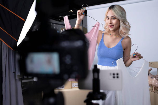 Młoda atrakcyjna azjatycka blogerka lub vlogger patrząc na aparat przeglądania produktu. Nowoczesna bizneswoman wykorzystująca media społecznościowe do marketingu. Biznes online influencer na koncepcji mediów społecznościowych. - Zdjęcie, obraz