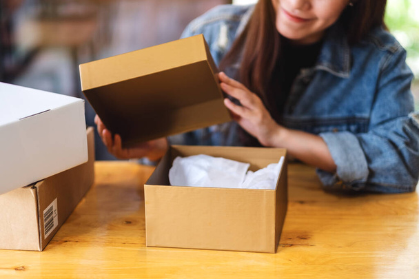 Eine schöne junge Asiatin erhält und öffnet zu Hause einen Postpaketkasten für die Zustellung und das Online-Shopping-Konzept - Foto, Bild