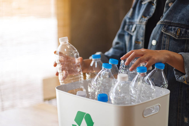 Een vrouw die recycleerbare plastic flessen inzamelt en scheidt in een vuilnisbak thuis - Foto, afbeelding
