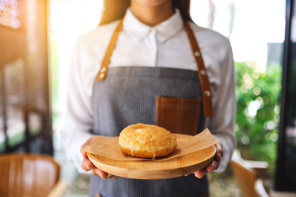 Σερβιτόρα που κρατάει και σερβίρει σπιτικό ντόνατ σε ξύλινο δίσκο - Φωτογραφία, εικόνα
