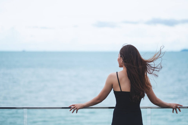 Visão traseira imagem de uma bela jovem mulher asiática de pé e olhando para o mar e céu azul  - Foto, Imagem