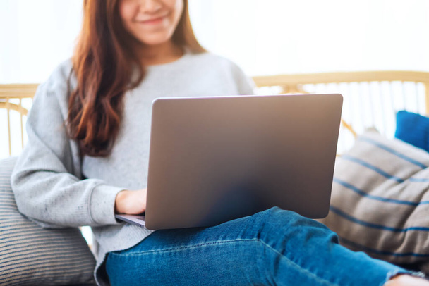 Een mooie vrouw met behulp van en werken op laptop computer terwijl liggend op een bank thuis - Foto, afbeelding