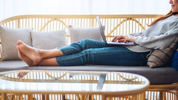 A beautiful woman using and working on laptop computer while lying on a sofa at home - Photo, Image