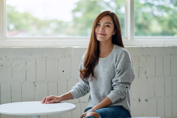 Portret beeld van een mooie jonge aziatische vrouw zitten in cafe met het gevoel gelukkig - Foto, afbeelding