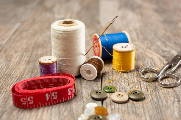 A closeup view of objects contained in a common sewing kit, featuring thread spools, tape measure, scissors, buttons and a needle. - Foto, Bild