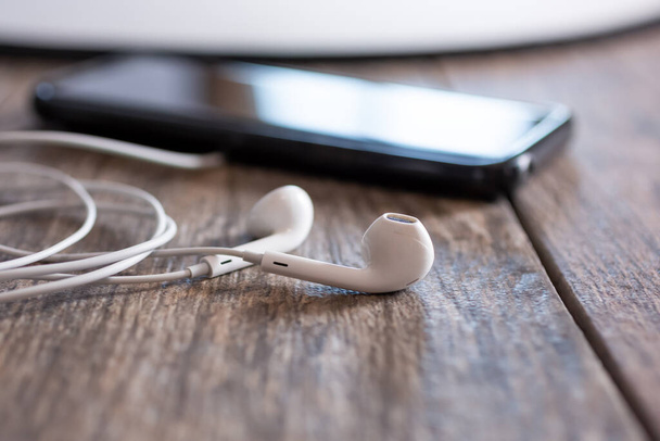A closeup view of a pair of white earbuds, adjacent a smart phone. - Foto, Imagen