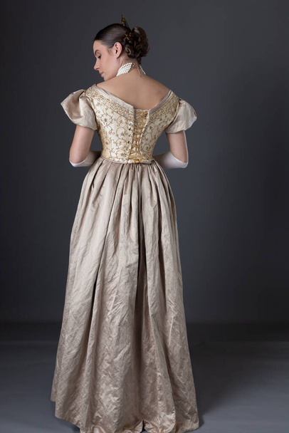 Вікторіанка, одягнена в золоту кулькову сукню з довгими, мереживними рукавичками, стоїть навпроти сірого фону. - Фото, зображення
