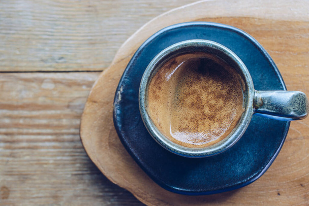 A cup of hot espresso shot on the wooden table. Espresso is a full-flavored It is made by forcing pressurized, hot water through very finely ground coffee beans. - Fotó, kép