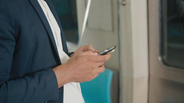 Close up businessman standing on the seat using modern smartphone to internet checking news on electric train, Passenger young man commuting texting on mobile phone by railway transport - Photo, image