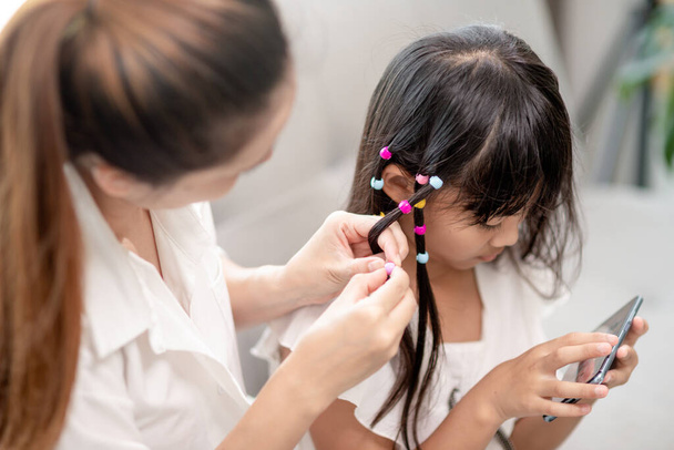 Young Asian mother tying daughter's hair - 写真・画像