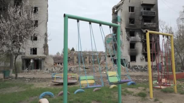 Детские качели на фоне разрушенного жилого здания в результате бомбардировки российской армией - Кадры, видео