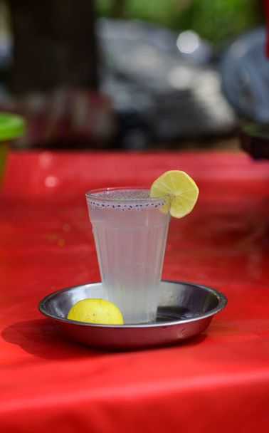 Glass of lime water or lemonade on a steel dish along with a piece of lime over a red  plastic top in a park - Photo, image