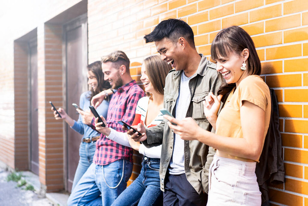 Amigos multiculturais rindo usando smartphone na parede no campus universitário - Jovens viciados em telefones inteligentes móveis - Conceito de tecnologia com sempre conectado - filtro brilhante - Foto, Imagem