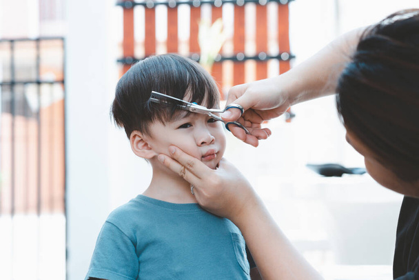 Madre asiatica taglia i capelli di suo figlio da sola a casa. Idee di taglio di capelli felici per i bambini. Le madri sono felici di tagliare i capelli dei loro figli. - Foto, immagini