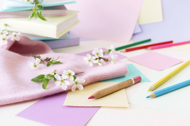 A stack of books, textbooks, pencils, notepads and twigs of cherry blossoms on a table, against a background of colored paper in pastel colors, the concept of learning, education, back to school  - Fotó, kép