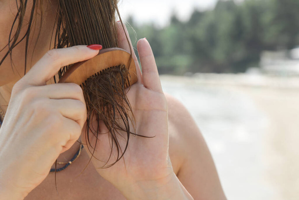 Cheveux de femme sur la plage. Femme apportant masque capillaire avec peigne en bois. Dommages aux cheveux dus à l'eau salée de l'océan et au soleil, concept de soins capillaires d'été. - Photo, image