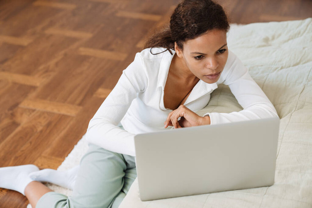 Mladá černošky žena pracuje s notebookem, zatímco sedí na podlaze doma - Fotografie, Obrázek