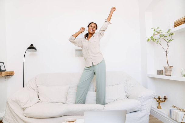 Young black woman dancing and smiling while listening music at home - Foto, imagen