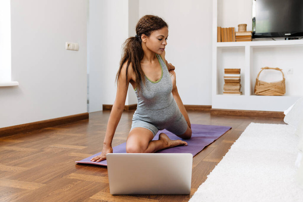Young black woman using laptop during yoga practice at home - Фото, зображення