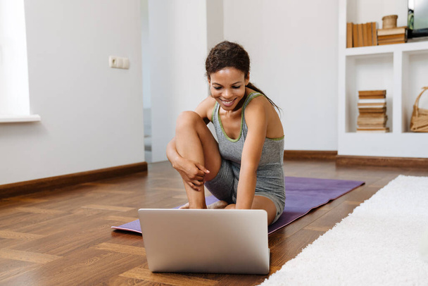 Young black woman using laptop during yoga practice at home - Фото, зображення