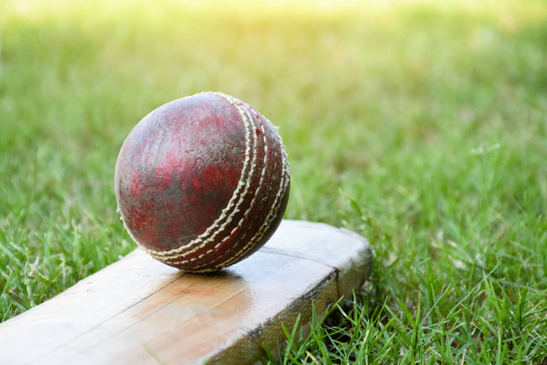 Старый красный кожаный крикетный мяч на летучей мыши для тренировок и тренировок на травяном полу рядом с кортом, мягкий и избирательный фокус на красный крикетный мяч. - Фото, изображение
