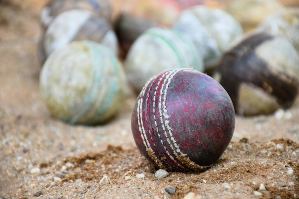 Alte Leder-Cricketbälle zum Training und Üben auf Sandboden neben dem Platz, weicher und selektiver Fokus auf roten Cricketball. - Foto, Bild