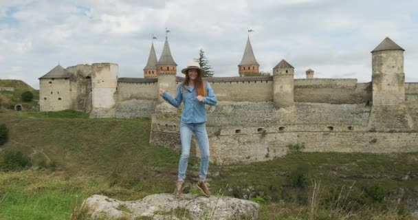 young girl jumps and dances against the backdrop of an old castle. Daytime, wide shot, Kamenetz Podolsk fortress. - Felvétel, videó