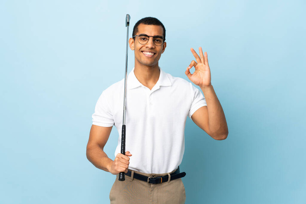 African American man over isolated blue background playing golf making OK sign - Foto, immagini
