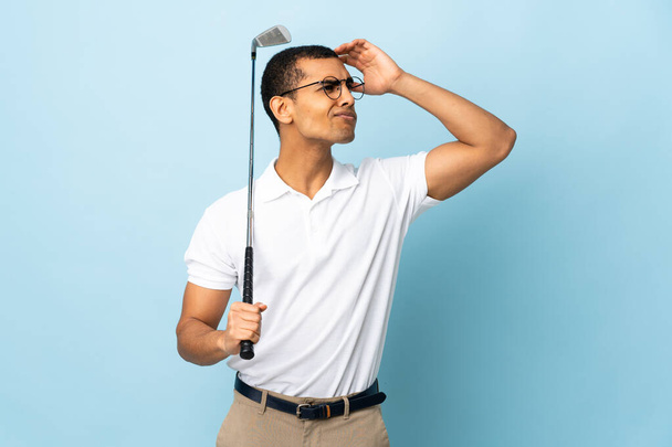 African American man over isolated blue background playing golf and and having doubts confuse face expression - Zdjęcie, obraz