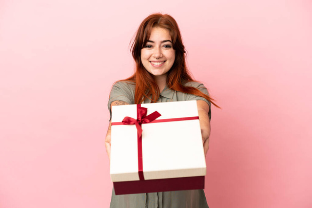 Young redhead caucasian woman isolated on pink background pregnant and holding a gift - Φωτογραφία, εικόνα