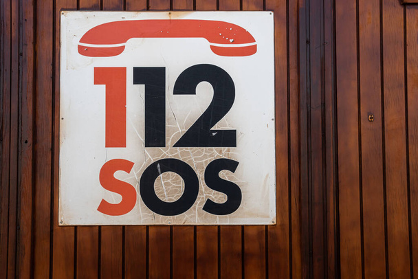 Gros plan d'un panneau d'urgence avec le numéro de téléphone 112 SOS, sur un fond en bois - Photo, image