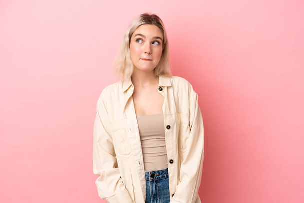 Young caucasian woman isolated on pink background having doubts while looking up - Foto, imagen