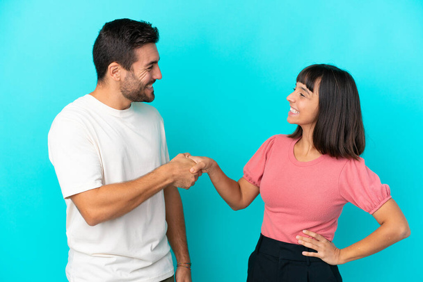 Young couple isolated on blue background handshaking after good deal - Φωτογραφία, εικόνα