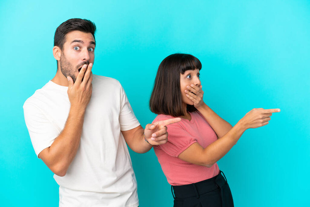 Young couple isolated on blue background pointing finger to the side with a surprised face - Photo, Image