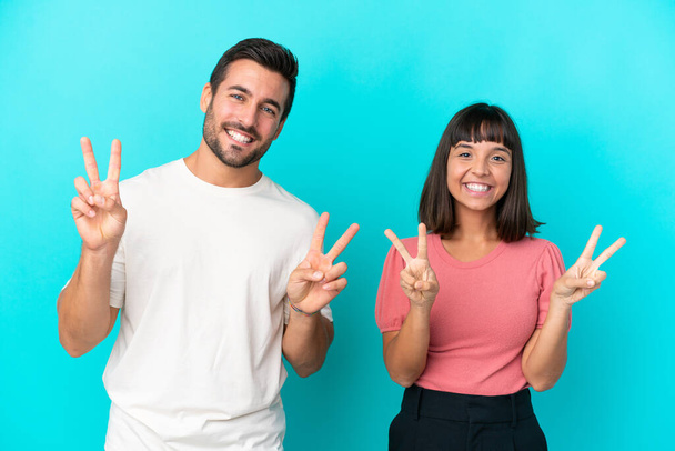 Young couple isolated on blue background smiling and showing victory sign with both hands - Φωτογραφία, εικόνα