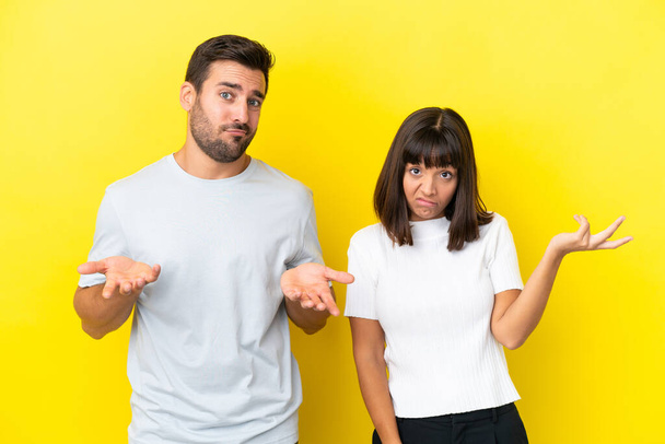 Young couple isolated on yellow background unhappy and frustrated with something because not understand something - Foto, Imagem