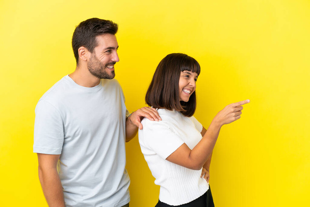 Young couple isolated on yellow background pointing to the side to present a product - Photo, Image