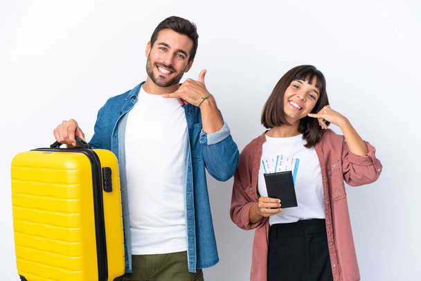 Młoda para podróżników trzymająca walizkę i paszport na białym tle, wykonująca gest telefoniczny. Oddzwoń. - Zdjęcie, obraz