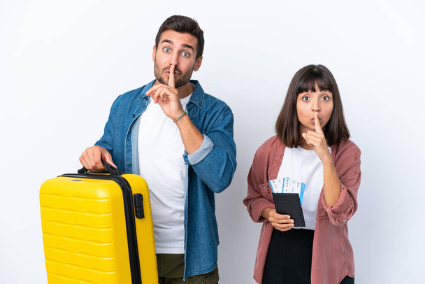Jonge reiziger paar met een koffer en paspoort geïsoleerd op witte achtergrond met een teken van stilte gebaar steek vinger in de mond - Foto, afbeelding