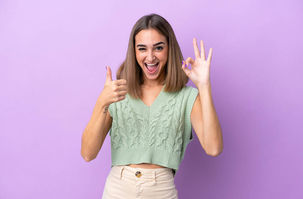 Young caucasian woman isolated on purple background showing ok sign and thumb up gesture - Photo, Image