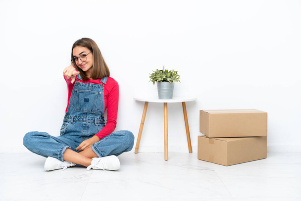 Young caucasian woman sitting on the floor among boxes points finger at you with a confident expression - Fotoğraf, Görsel